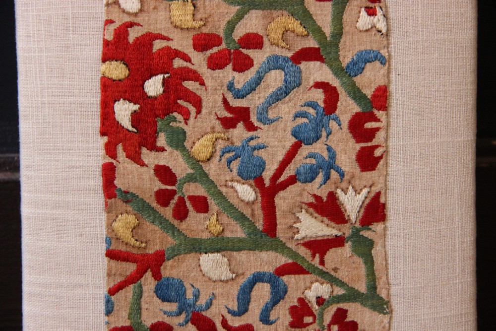 An antique Greek Skyros embroidery fragment stitched with red, blue, green, and yellow silk thread floral patterns, mounted on a neutral linen display board. View II