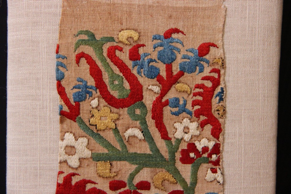 An antique Greek Skyros embroidery fragment stitched with red, blue, green, and yellow silk thread floral patterns, mounted on a neutral linen display board. View III