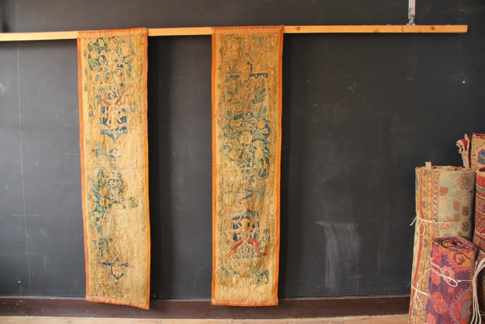 A pair of long vertical 17th-century woven tapestry borders featuring botanical foliage, urns, and floral motifs in yellow, green, and blue tones. View III