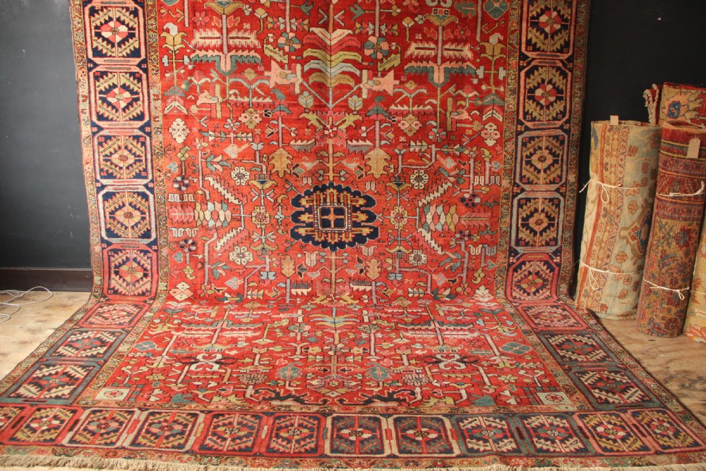 A large hand-knotted antique Heriz carpet with a rich terracotta red field, geometric floral motifs, and a navy blue central medallion. View II
