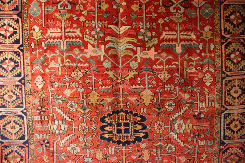 A large hand-knotted antique Heriz carpet with a rich terracotta red field, geometric floral motifs, and a navy blue central medallion. View III