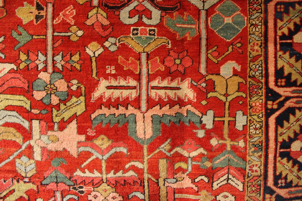 A large hand-knotted antique Heriz carpet with a rich terracotta red field, geometric floral motifs, and a navy blue central medallion. View V