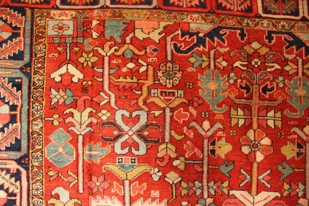 A large hand-knotted antique Heriz carpet with a rich terracotta red field, geometric floral motifs, and a navy blue central medallion. View VII