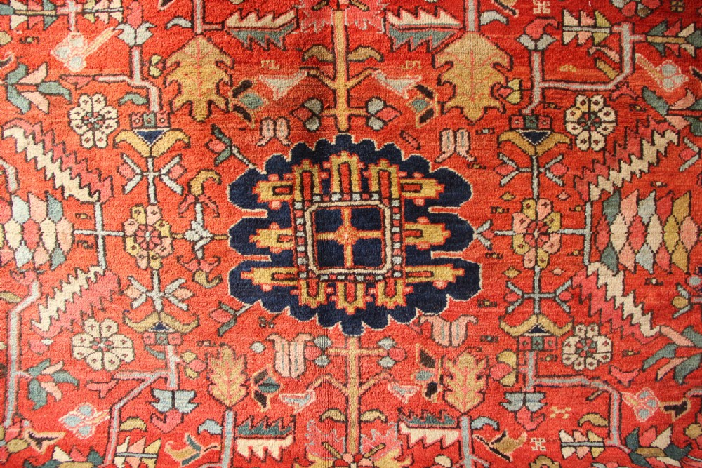 A large hand-knotted antique Heriz carpet with a rich terracotta red field, geometric floral motifs, and a navy blue central medallion. View VIII