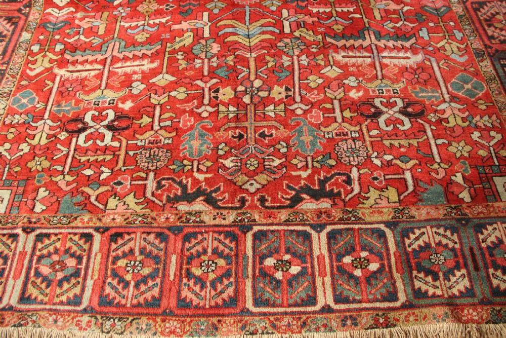 A large hand-knotted antique Heriz carpet with a rich terracotta red field, geometric floral motifs, and a navy blue central medallion. View IX