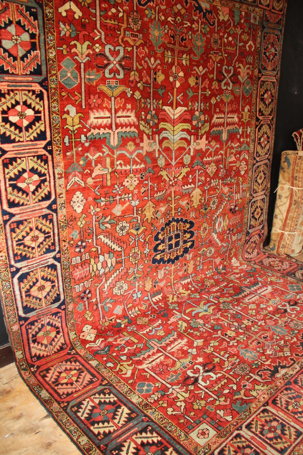 A large hand-knotted antique Heriz carpet with a rich terracotta red field, geometric floral motifs, and a navy blue central medallion. View XI