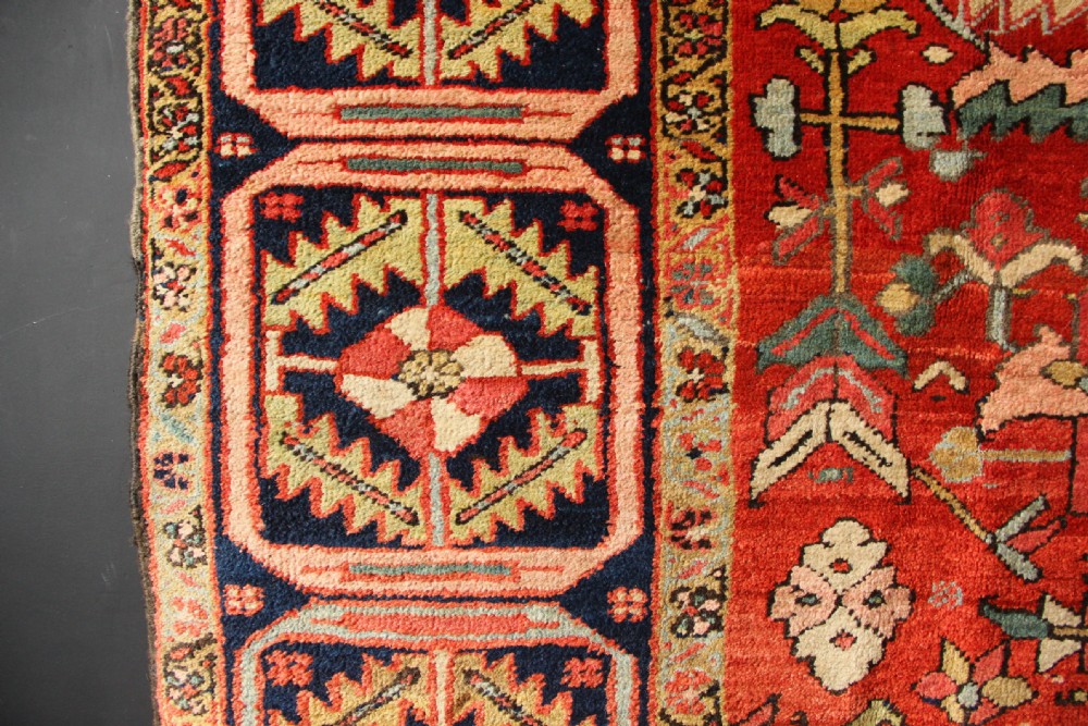 A large hand-knotted antique Heriz carpet with a rich terracotta red field, geometric floral motifs, and a navy blue central medallion. View XII