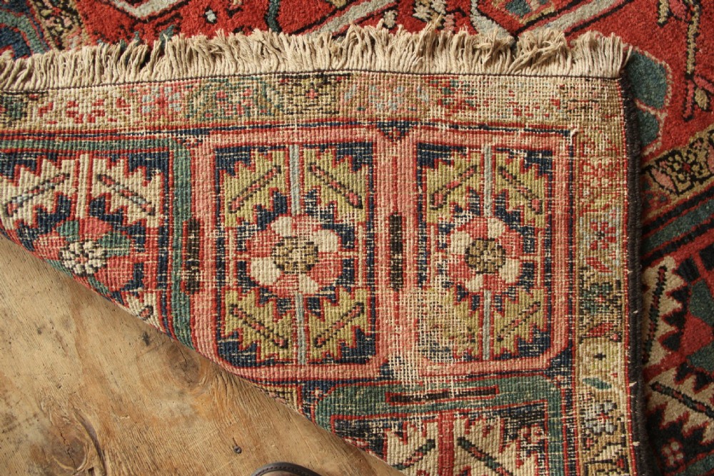 A large hand-knotted antique Heriz carpet with a rich terracotta red field, geometric floral motifs, and a navy blue central medallion. View XIV