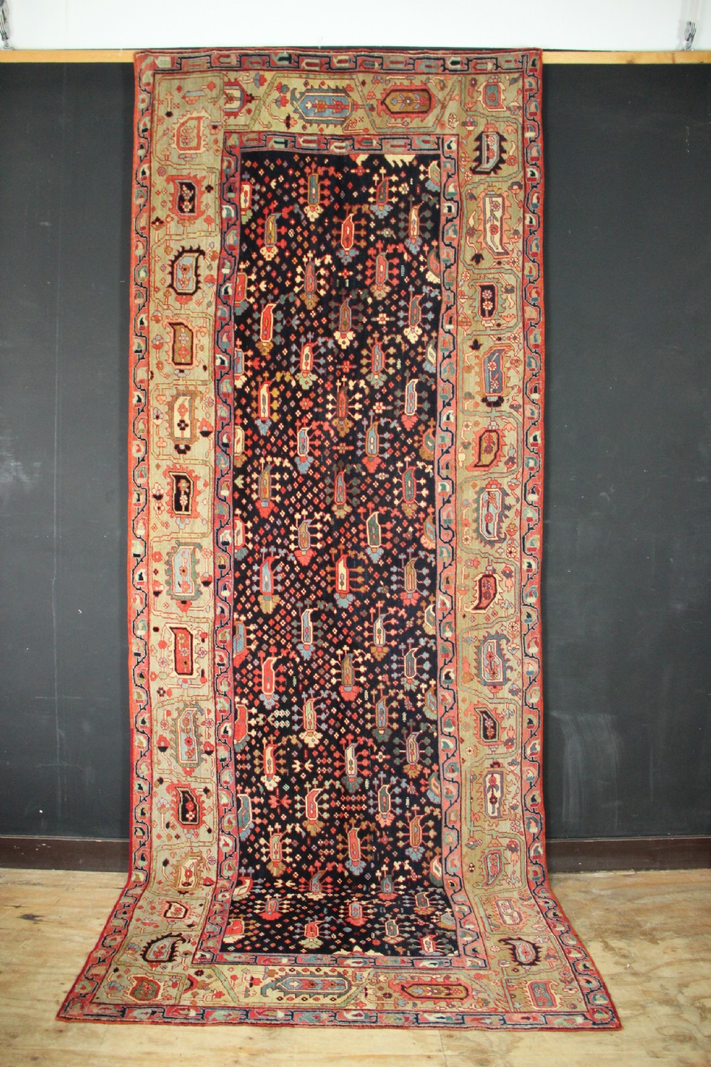 An antique Persian Serapi gallery carpet with a navy blue field featuring repeating boteh motifs framed by a wide sage green ornamental border.