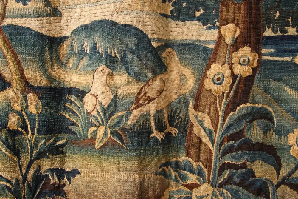 An 18th-century hand-woven Flemish verdure tapestry depicting a dense woodland scene with birds and a floral border in shades of green, cream, and brown. View III
