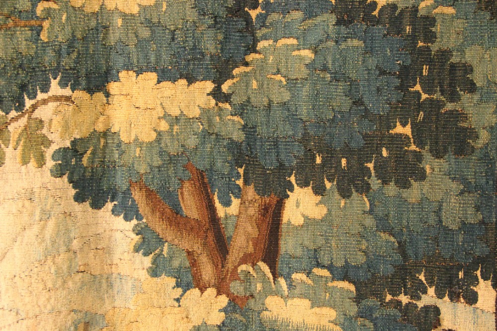 An 18th-century hand-woven Flemish verdure tapestry depicting a dense woodland scene with birds and a floral border in shades of green, cream, and brown. View IV
