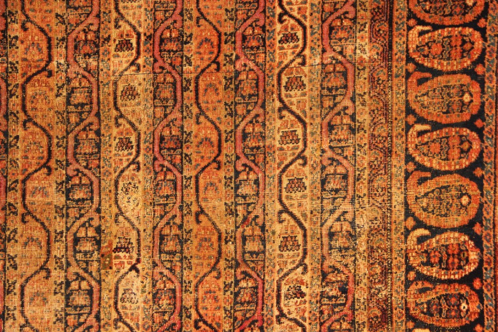 A large rectangular antique Persian Khorassan wool carpet featuring vertical striped pattern bands framed by a dark navy border filled with repeating boteh paisley motifs in rust and ochre tones. View VII