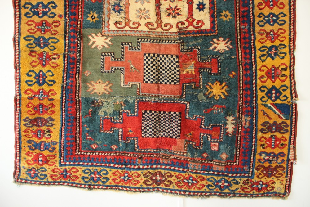 An antique hand-knotted Caucasian Kazak rug remnant featuring geometric stepped medallions and a patterned yellow border. View II