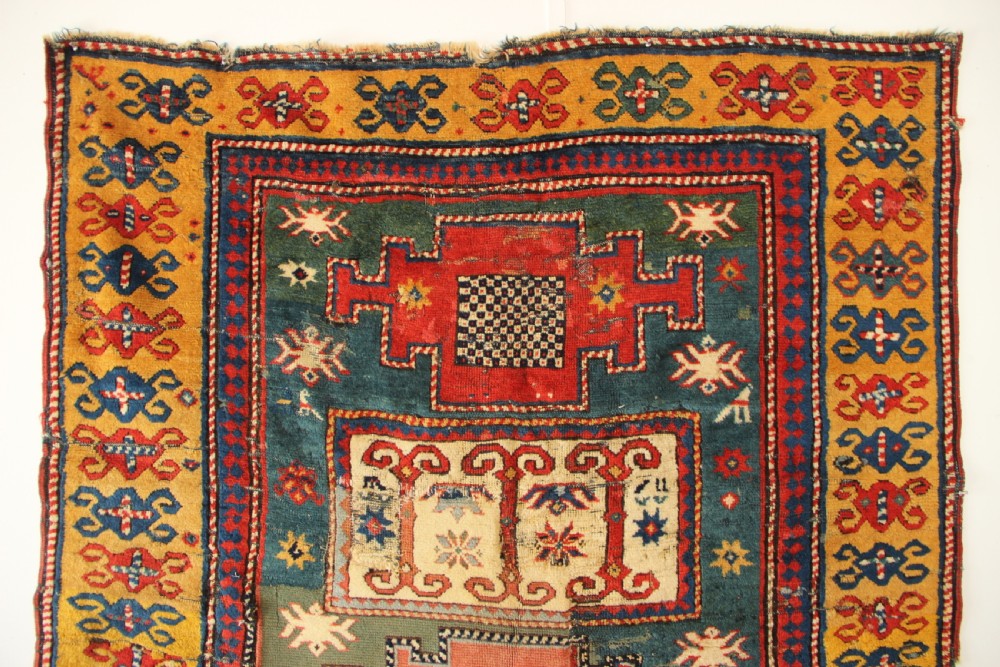 An antique hand-knotted Caucasian Kazak rug remnant featuring geometric stepped medallions and a patterned yellow border. View III