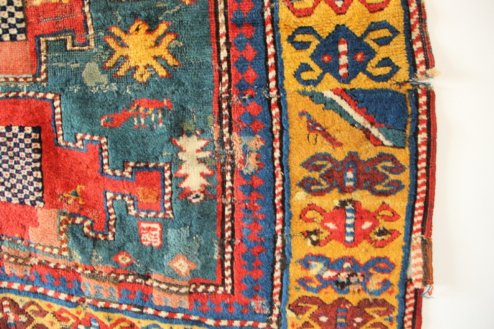 An antique hand-knotted Caucasian Kazak rug remnant featuring geometric stepped medallions and a patterned yellow border. View V