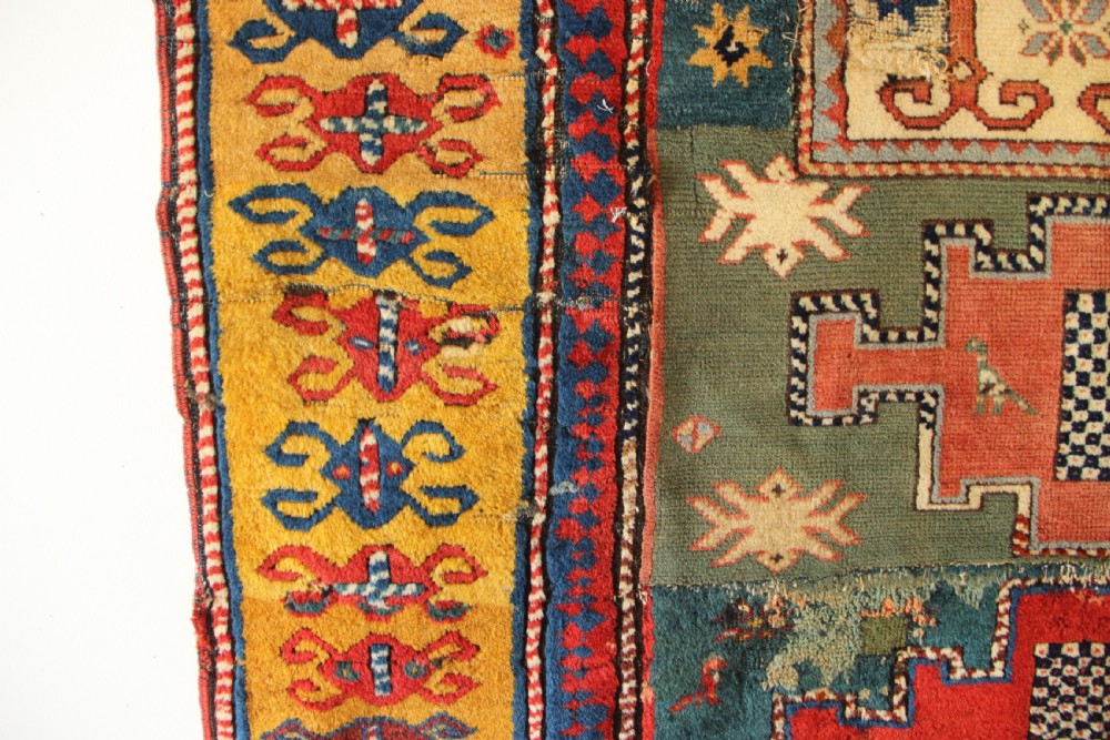An antique hand-knotted Caucasian Kazak rug remnant featuring geometric stepped medallions and a patterned yellow border. View VI