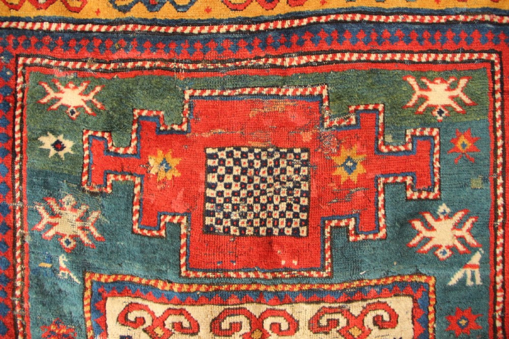 An antique hand-knotted Caucasian Kazak rug remnant featuring geometric stepped medallions and a patterned yellow border. View VII