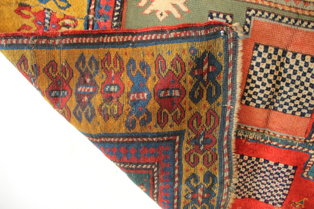 An antique hand-knotted Caucasian Kazak rug remnant featuring geometric stepped medallions and a patterned yellow border. View VIII
