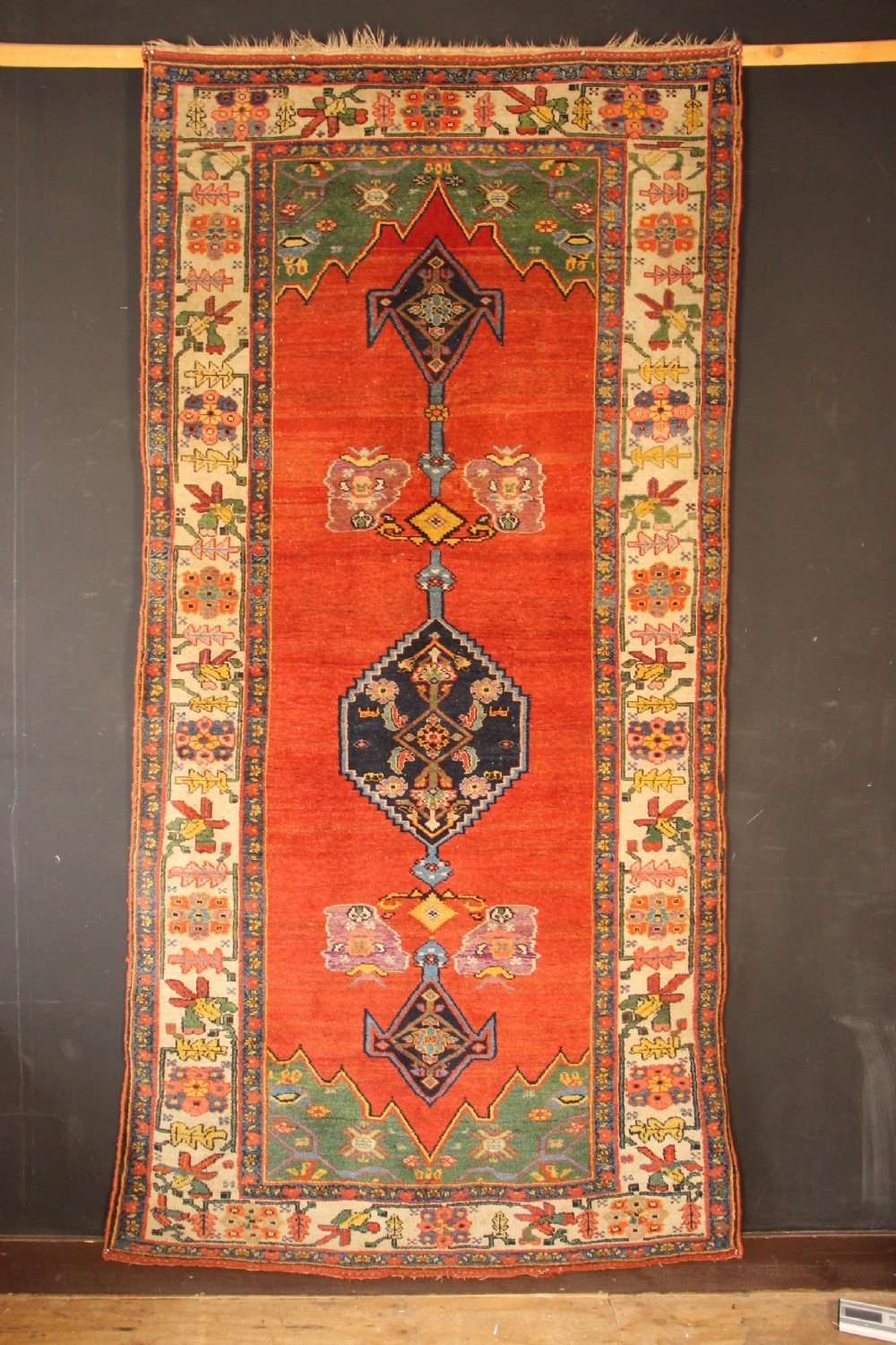 An antique long Bidjar carpet featuring a terracotta red field with central navy geometric medallions, green corner spandrels, and a cream floral border.