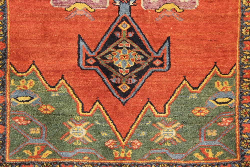 An antique long Bidjar carpet featuring a terracotta red field with central navy geometric medallions, green corner spandrels, and a cream floral border. View III