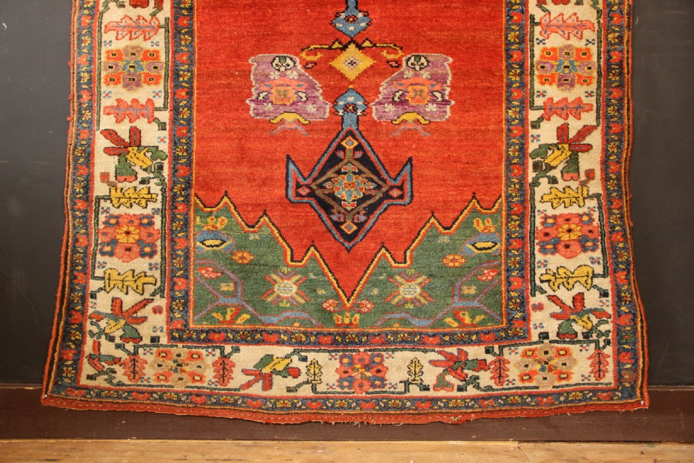 An antique long Bidjar carpet featuring a terracotta red field with central navy geometric medallions, green corner spandrels, and a cream floral border. View V