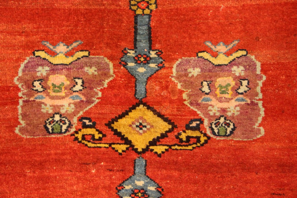 An antique long Bidjar carpet featuring a terracotta red field with central navy geometric medallions, green corner spandrels, and a cream floral border. View VII