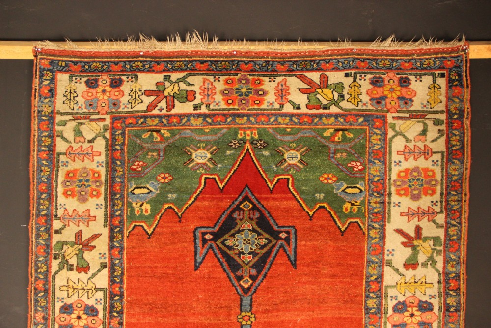 An antique long Bidjar carpet featuring a terracotta red field with central navy geometric medallions, green corner spandrels, and a cream floral border. View VIII