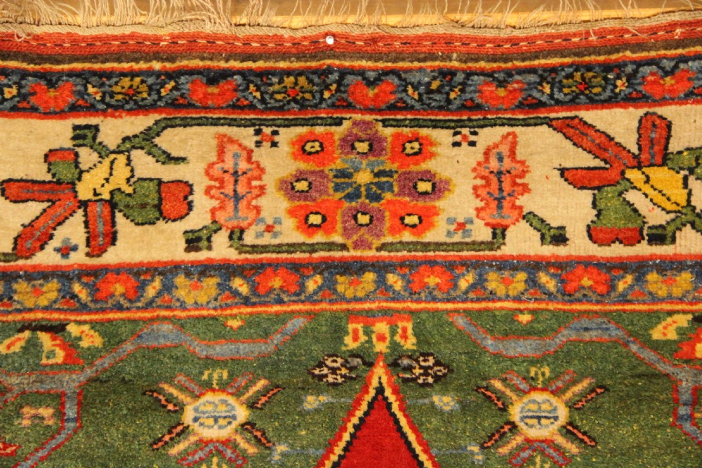 An antique long Bidjar carpet featuring a terracotta red field with central navy geometric medallions, green corner spandrels, and a cream floral border. View IX