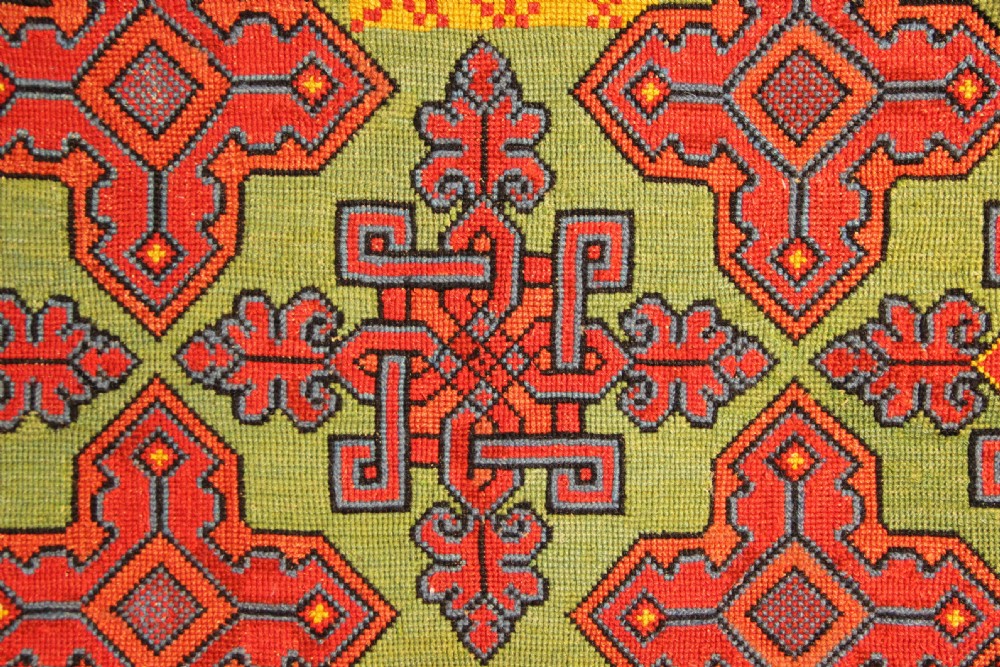 A rectangular 19th-century Swedish wool embroidery featuring geometric and floral motifs in red, orange, and blue against a green background, inscribed with the year 1843. View II