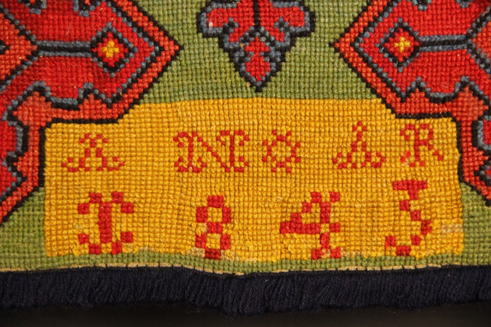 A rectangular 19th-century Swedish wool embroidery featuring geometric and floral motifs in red, orange, and blue against a green background, inscribed with the year 1843. View III