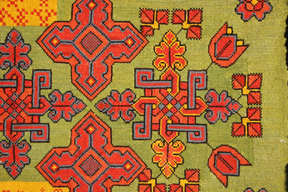 A rectangular 19th-century Swedish wool embroidery featuring geometric and floral motifs in red, orange, and blue against a green background, inscribed with the year 1843. View V