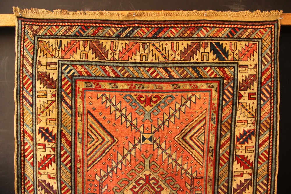 An antique hand-knotted Caucasian Shirvan wool rug with geometric diamond medallions in shades of terracotta, blue, red, and cream. View III