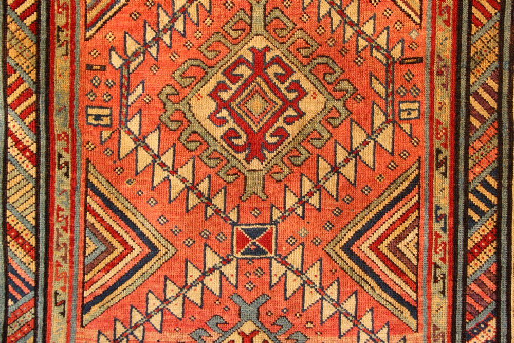 An antique hand-knotted Caucasian Shirvan wool rug with geometric diamond medallions in shades of terracotta, blue, red, and cream. View V