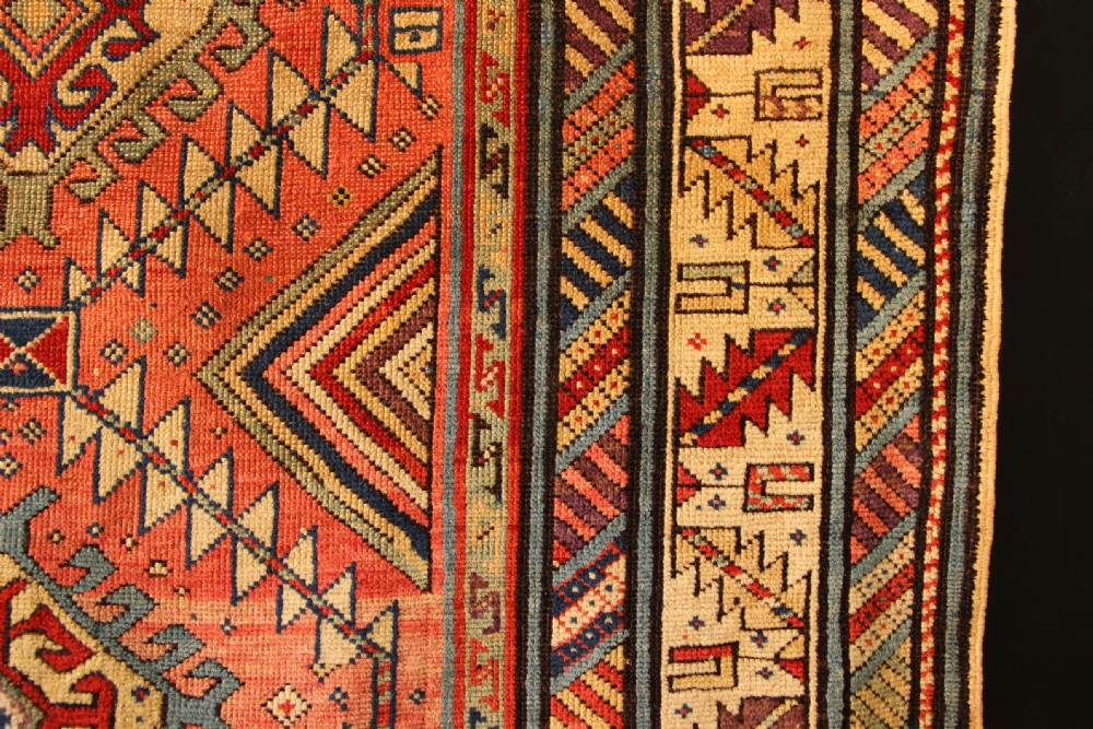 An antique hand-knotted Caucasian Shirvan wool rug with geometric diamond medallions in shades of terracotta, blue, red, and cream. View VI