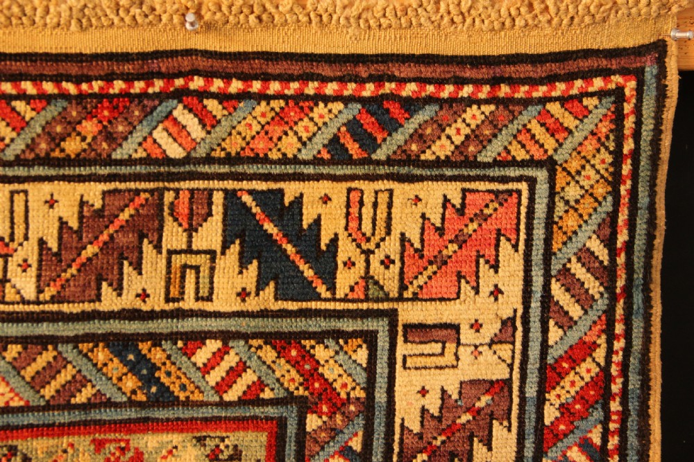 An antique hand-knotted Caucasian Shirvan wool rug with geometric diamond medallions in shades of terracotta, blue, red, and cream. View VII
