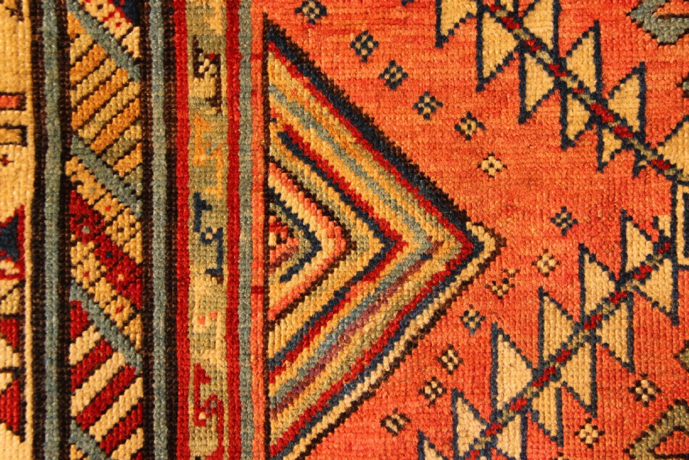 An antique hand-knotted Caucasian Shirvan wool rug with geometric diamond medallions in shades of terracotta, blue, red, and cream. View VIII