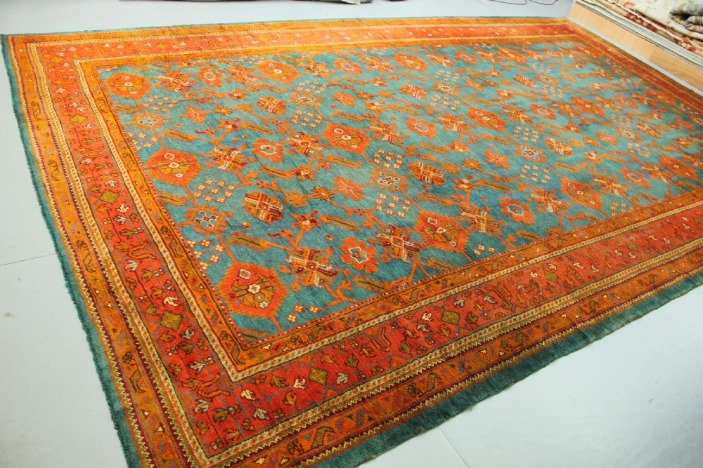 An antique Oushak wool rug displaying a teal field with geometric orange motifs and multi-layered terracotta borders. View VI