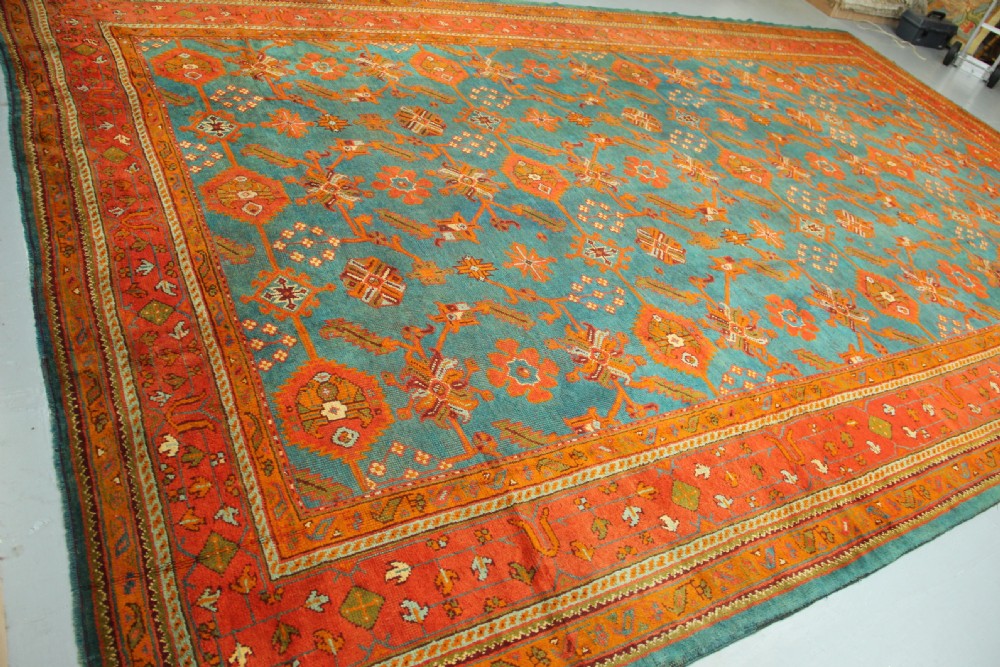An antique Oushak wool rug displaying a teal field with geometric orange motifs and multi-layered terracotta borders. View VII
