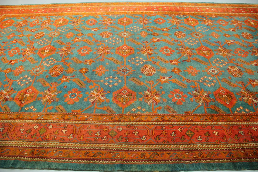 An antique Oushak wool rug displaying a teal field with geometric orange motifs and multi-layered terracotta borders. View VIII