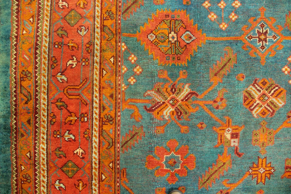 An antique Oushak wool rug displaying a teal field with geometric orange motifs and multi-layered terracotta borders. View XII