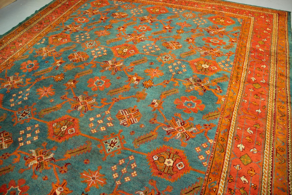 An antique Oushak wool rug displaying a teal field with geometric orange motifs and multi-layered terracotta borders. View XIII