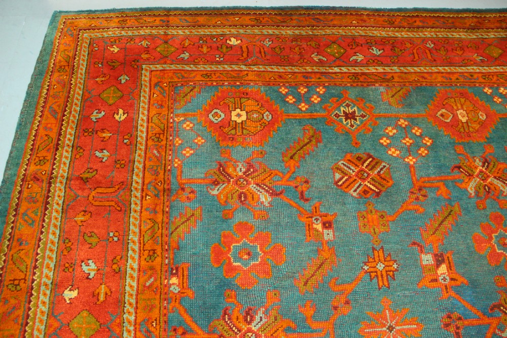 An antique Oushak wool rug displaying a teal field with geometric orange motifs and multi-layered terracotta borders. View XIV