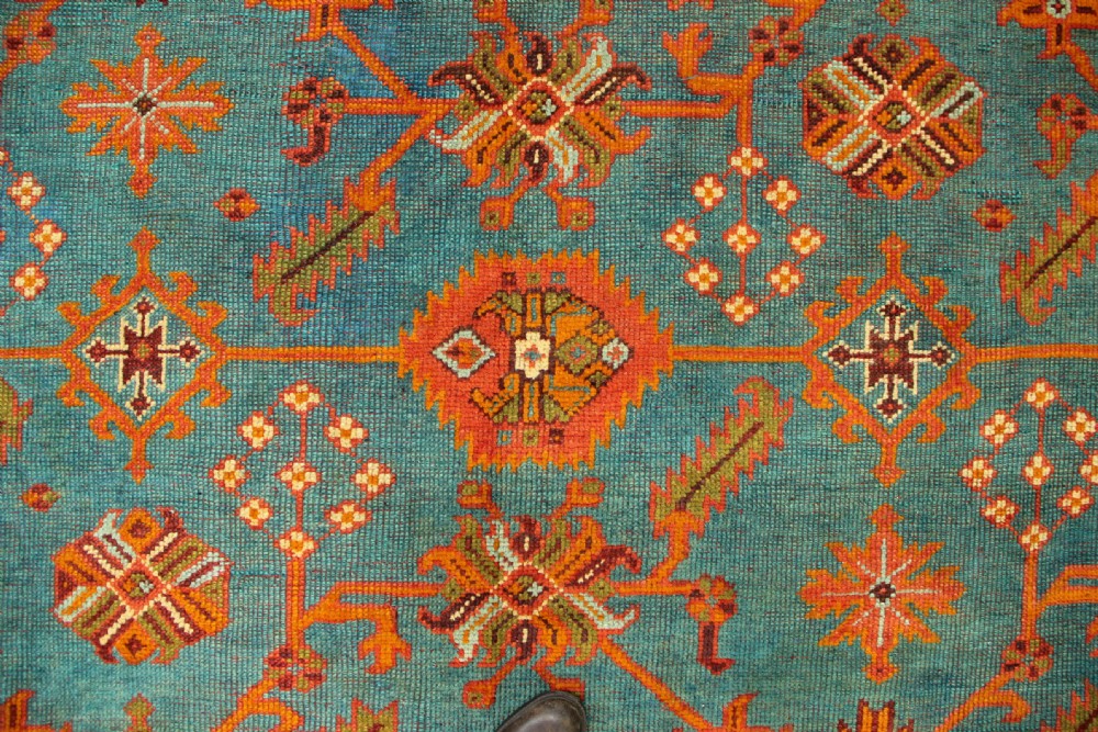 An antique Oushak wool rug displaying a teal field with geometric orange motifs and multi-layered terracotta borders. View XV
