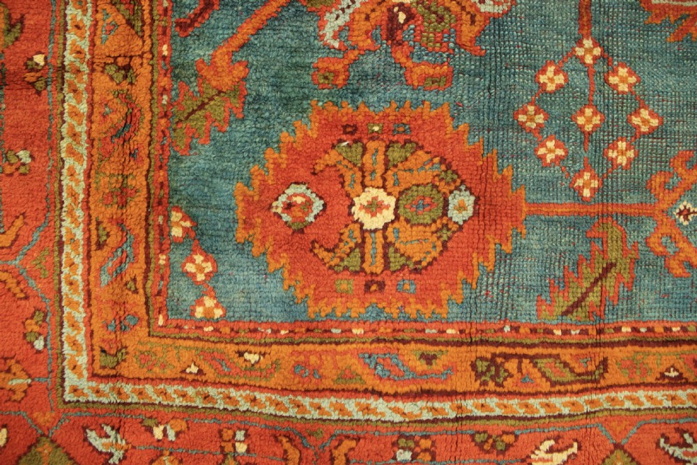 An antique Oushak wool rug displaying a teal field with geometric orange motifs and multi-layered terracotta borders. View XVI