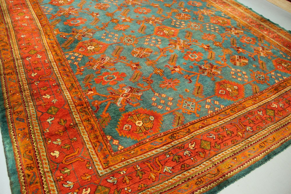 An antique Oushak wool rug displaying a teal field with geometric orange motifs and multi-layered terracotta borders. View XVII