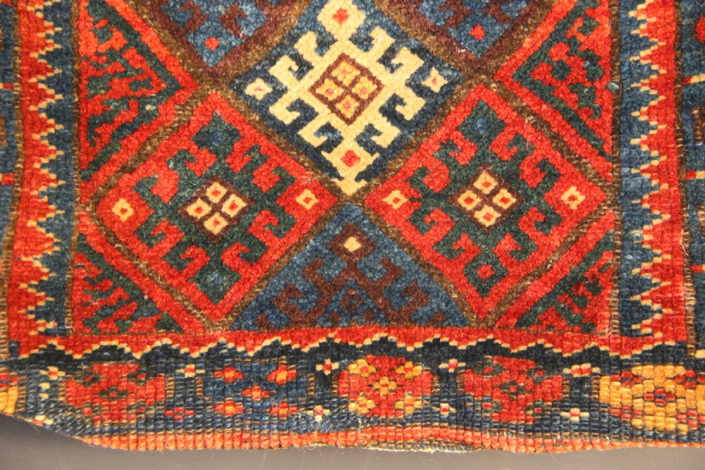 An antique handwoven Jaf Kurd wool saddlebag face featuring diamond latch-hook medallions in red, blue, and yellow. View V