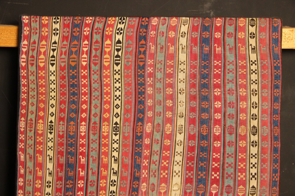 A rectangular mounted 19th-century silk jajim textile featuring vertical stripes with intricate geometric and stylized animal motifs in red, blue, cream, and yellow hues. View II