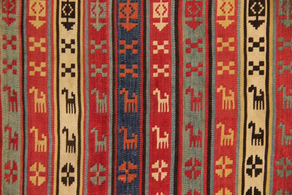 A rectangular mounted 19th-century silk jajim textile featuring vertical stripes with intricate geometric and stylized animal motifs in red, blue, cream, and yellow hues. View IV