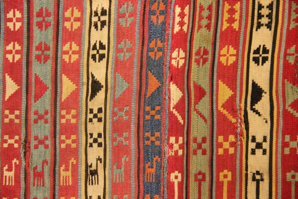 A rectangular mounted 19th-century silk jajim textile featuring vertical stripes with intricate geometric and stylized animal motifs in red, blue, cream, and yellow hues. View V