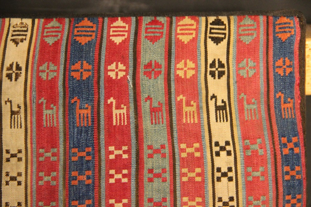 A rectangular mounted 19th-century silk jajim textile featuring vertical stripes with intricate geometric and stylized animal motifs in red, blue, cream, and yellow hues. View VI
